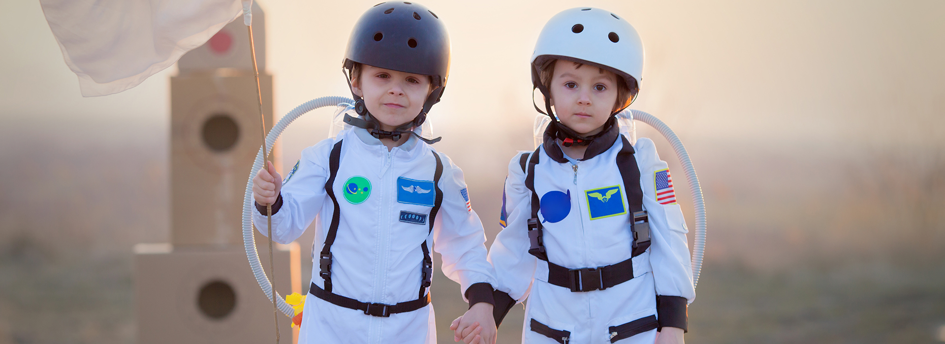 Two adorable children, boy brothers, playing in park on sunset, dressed like astronauts, imagining they are flying on the moon
